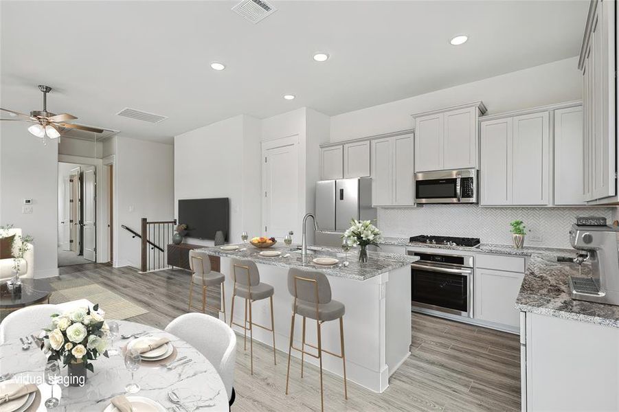 Kitchen featuring ceiling fan, an island with sink, appliances with stainless steel finishes, light stone countertops, and light hardwood / wood-style floors