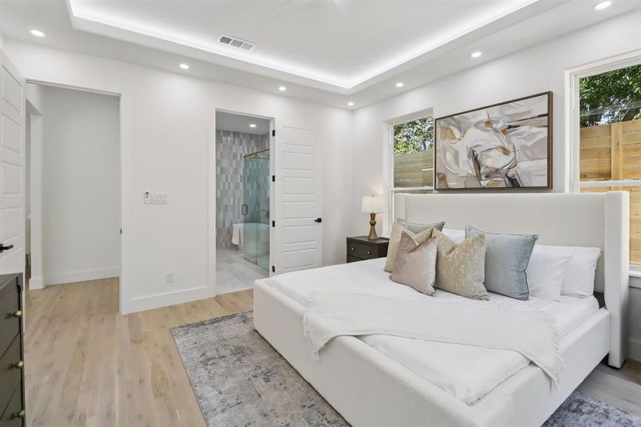 Bedroom with recessed lighting, light wood-type flooring, a tray ceiling, and ensuite bathroom