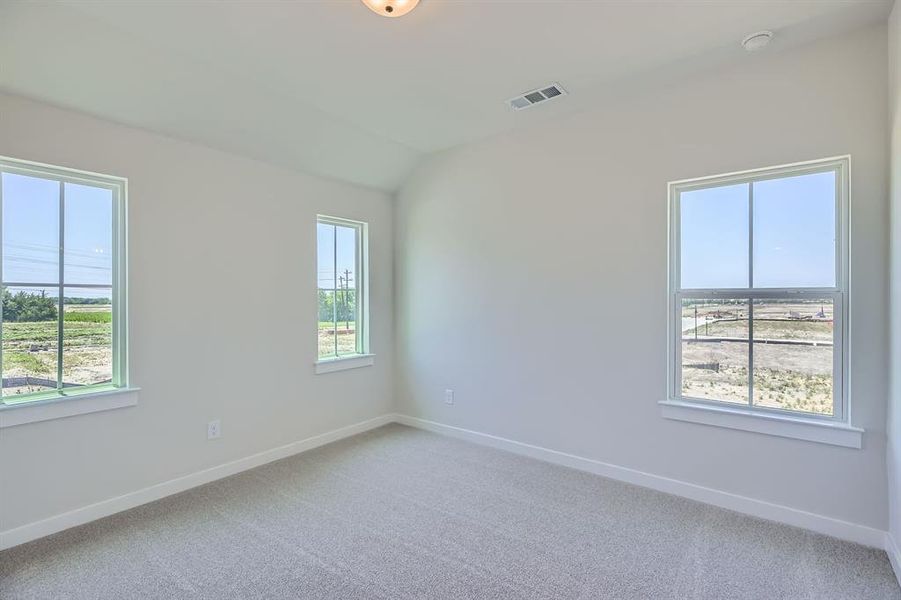 Empty room with plenty of natural light, baseboards, light colored carpet, lofted ceiling, and a smoke detector Empty room with plenty of natural light, baseboards, light colored carpet, lofted ceiling, and a smoke detector
