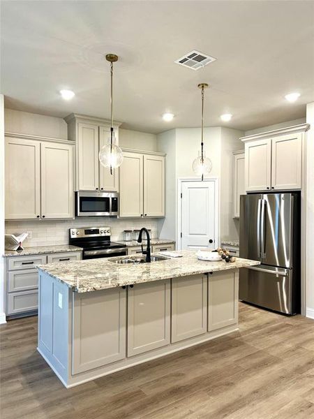 Kitchen featuring stainless steel appliances, a sink, a kitchen island with sink, light wood-style floors, and pendant lighting Kitchen featuring stainless steel appliances, a sink, a kitchen island with sink, light wood-style floors, and pendant lighting