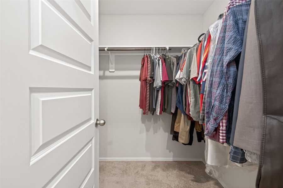 This photo shows a walk-in closet with ample hanging space for clothes, featuring a clean, carpeted floor and white walls, providing a neat and organized storage solution.
