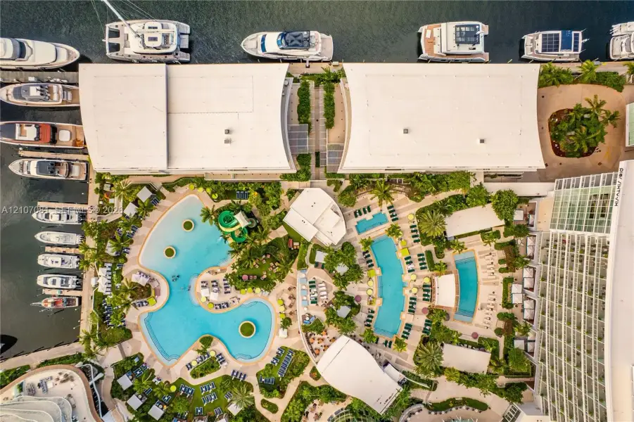 Aerial perspective of a waterfront property featuring multiple swimming pools, paved pool decks, lush landscaped grounds, and direct marina access Aerial perspective of a waterfront property featuring multiple swimming pools, paved pool decks, lush landscaped grounds, and direct marina access