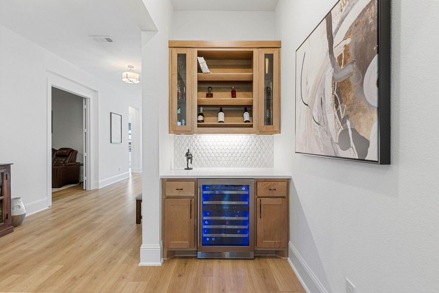 Beautifully designed dry bar with custom cabinetry and textured tile backsplash adding convenience and style to the home.