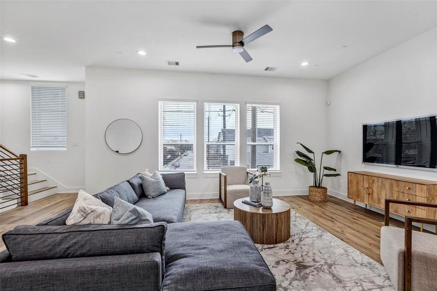 Bright and inviting living room, filled with natural light from large side windows, offering a glimpse of the peaceful neighborhood just outside.