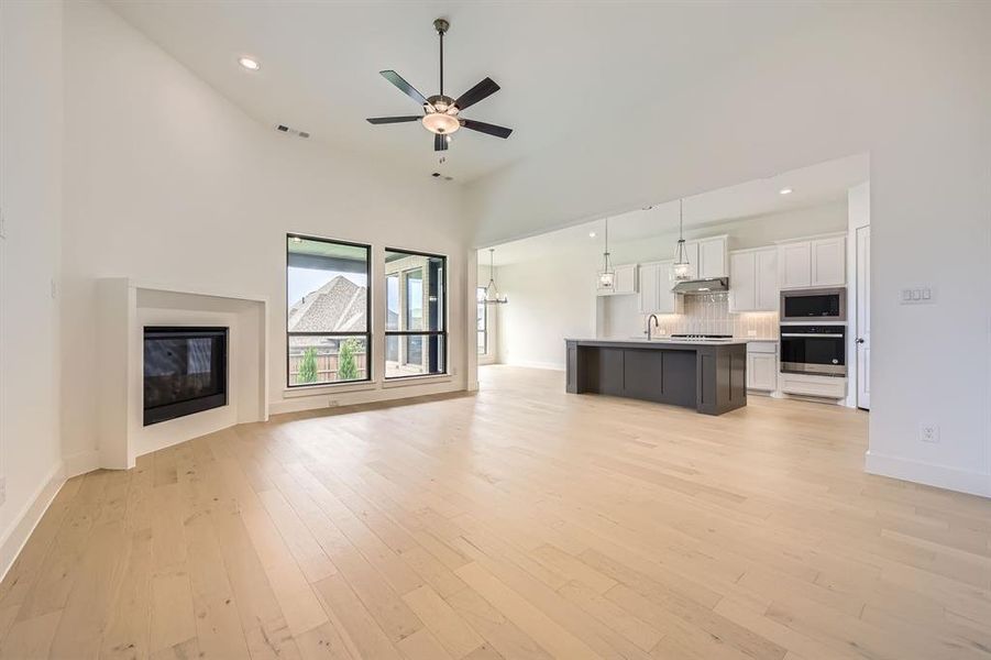 Unfurnished living room featuring a glass covered fireplace, a high ceiling, ceiling fan, light wood-style floors, and hanging lights
