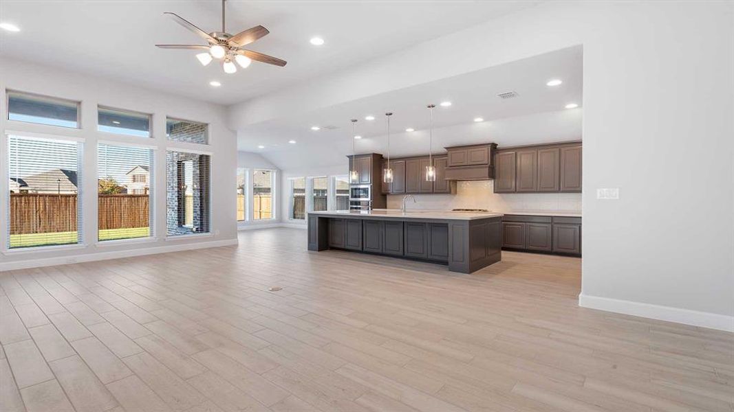 Kitchen featuring ceiling fan, sink, decorative light fixtures, a center island with sink, and light wood-type flooring