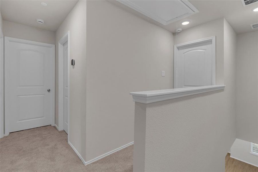 This image shows a well-lit, neutral-toned hallway space with carpeted flooring, featuring an inset nook with a ledge and recessed lighting. White doors leading to the bedrooms!