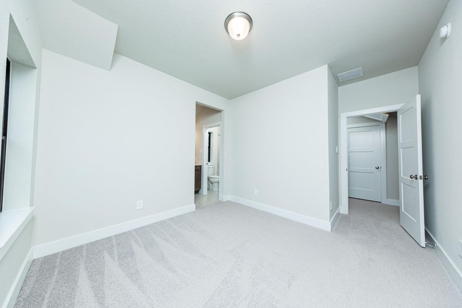 This inviting secondary bedroom combines comfort and modern elegance, featuring plush carpeting, a neutral color palette, and abundant natural light streaming through a large window. Discover the efficiency and convenience of accessing the secondary bathroom with another secondary bedroom--a highly functional solution for busy families.