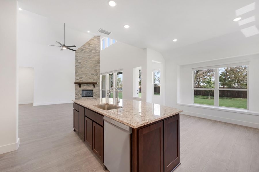 Kitchen island with granite countertop and sink, open to living area with stone fireplace and vaulted ceiling