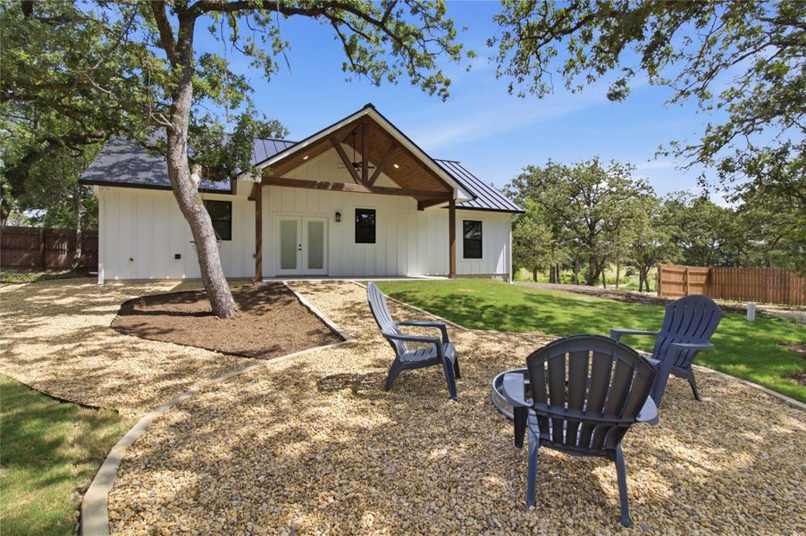 A striking modern farmhouse boasts a welcoming covered patio and a charming gravel yard with mature trees. A striking modern farmhouse boasts a welcoming covered patio and a charming gravel yard with mature trees.
