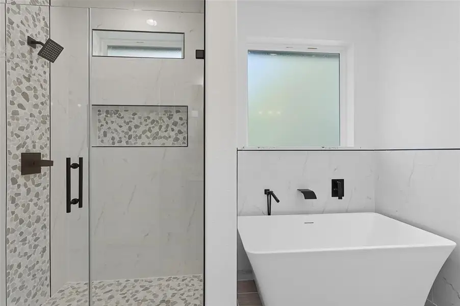 Full bathroom featuring a marble finish shower, a freestanding bath, and tile walls Full bathroom featuring a marble finish shower, a freestanding bath, and tile walls