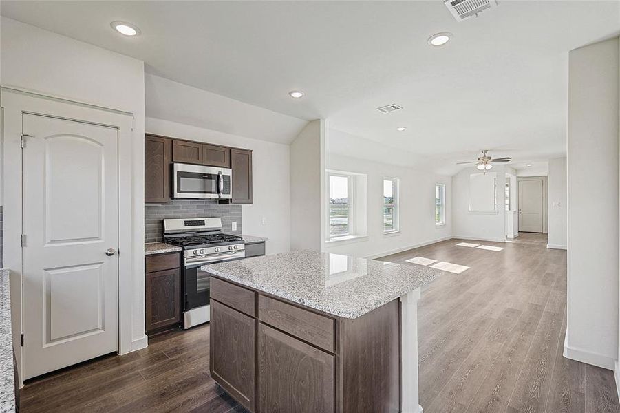 Kitchen featuring decorative backsplash, appliances with stainless steel finishes, wood-type flooring, and ceiling fan