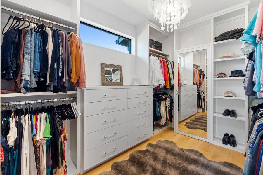 Custom closet system featuring extensive shelving, hanging rods, built-in drawer storage, hardwood-style flooring, and a full-length mirror
