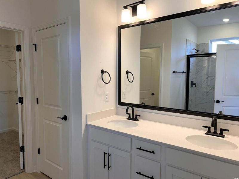 Bathroom featuring double vanity, a marble finish shower, and a spacious closet