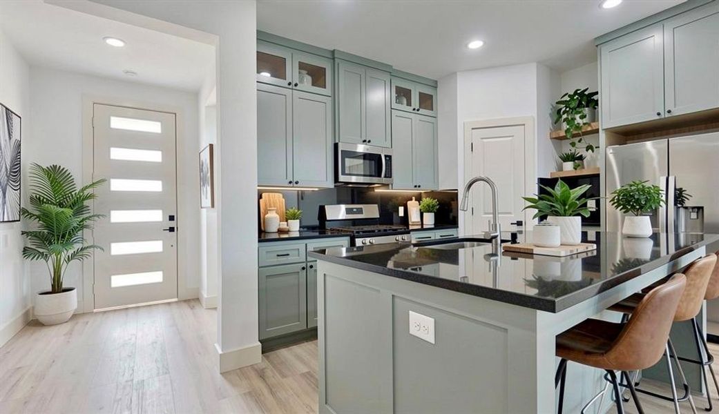Kitchen featuring stainless steel appliances, a breakfast bar, light wood-style floors, dark stone countertops, and an island with sink