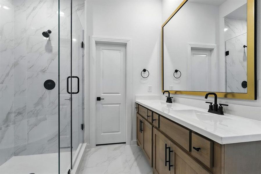 Full bath featuring light marble finish floors, a marble finish shower, and double vanity Full bath featuring light marble finish floors, a marble finish shower, and double vanity