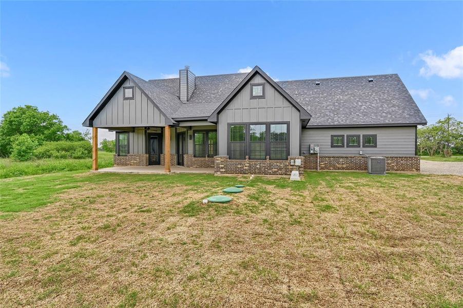 Back of property featuring a shingled roof, board and batten siding, a yard, and a chimney