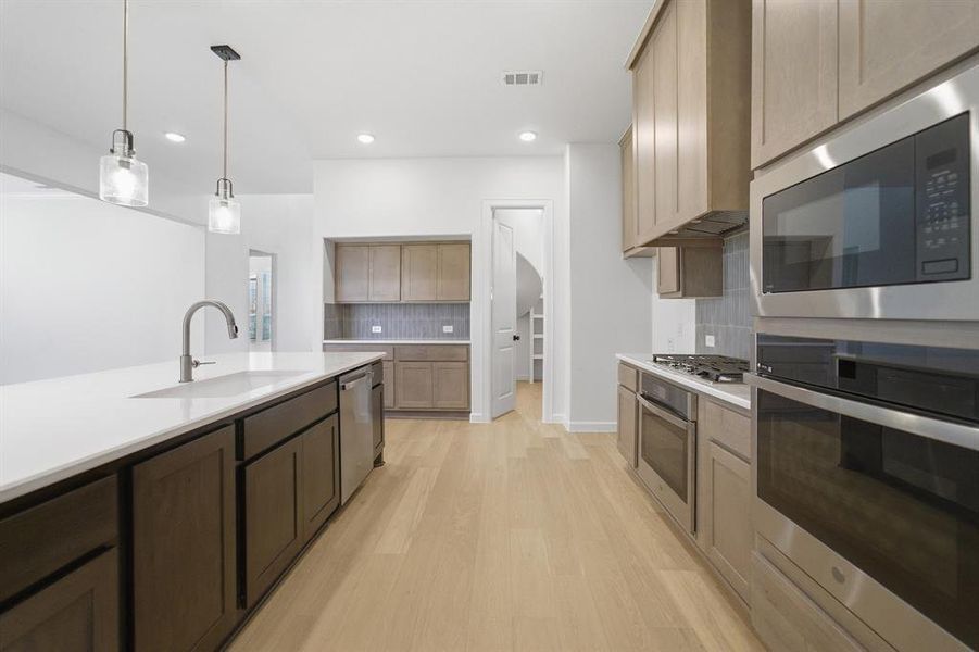 Gourmet kitchen featuring a large island with white countertop, stainless steel sink with gooseneck faucet, light wood-finish flooring, built-in stainless steel appliances, and recessed lighting
