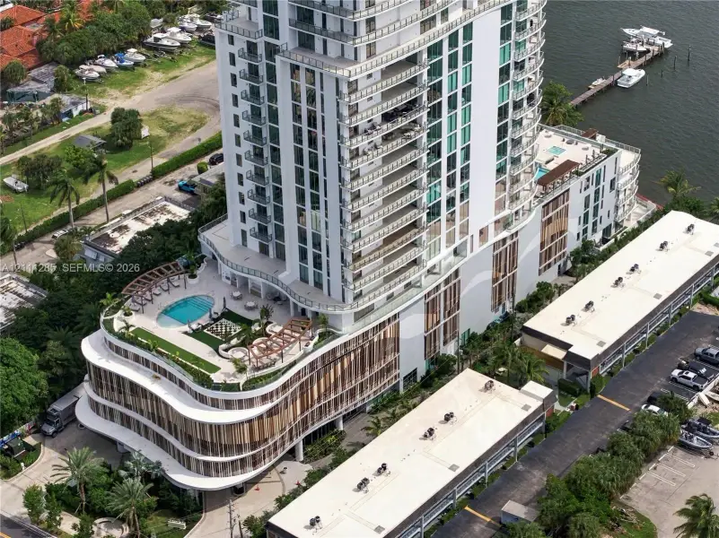 High-rise residential tower featuring a multi-level structure, wraparound balconies, an elevated swimming pool with a sprawling sun deck, and integrated waterfront access High-rise residential tower featuring a multi-level structure, wraparound balconies, an elevated swimming pool with a sprawling sun deck, and integrated waterfront access