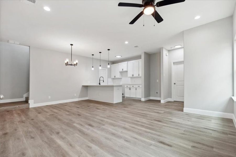 Unfurnished living room featuring sink, light hardwood / wood-style flooring, and ceiling fan with notable chandelier