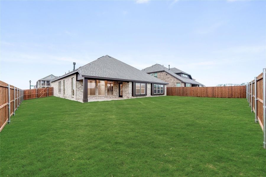 Brick home rear view with large fenced backyard, covered patio, and green lawn