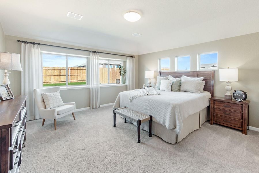 Spacious master bedroom with wood headboard, carpet flooring, and large windows with white curtains Spacious master bedroom with wood headboard, carpet flooring, and large windows with white curtains