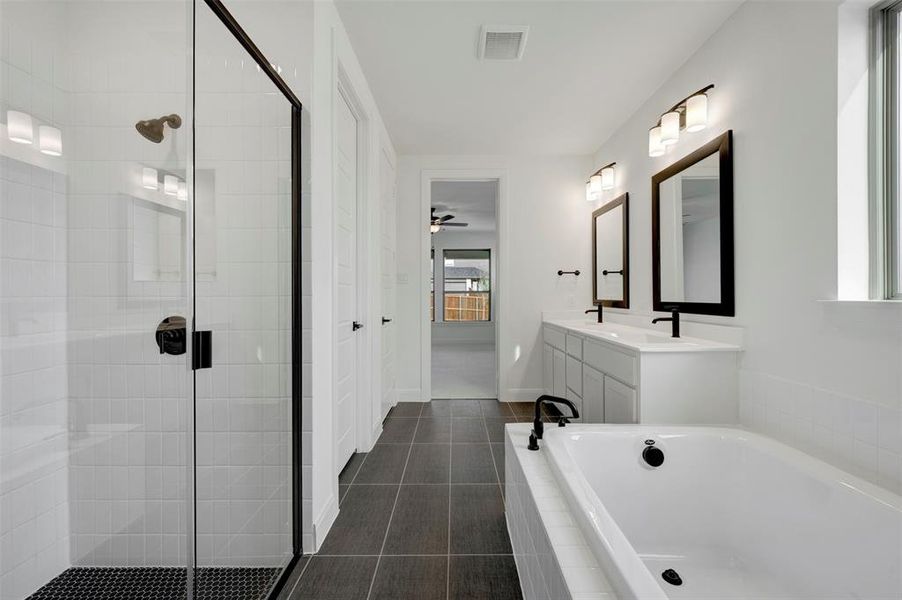 Full bath featuring double vanity, a bath, a stall shower, dark tile patterned flooring, and a ceiling fan