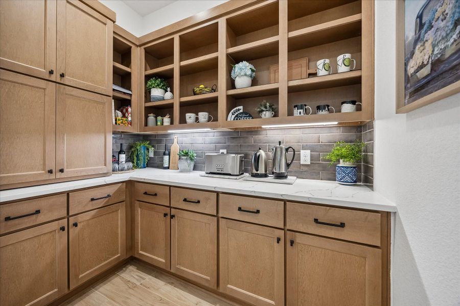 This upgraded extended pantry/coffee bar, located just off the kitchen, features elegant granite countertops, a designer earth-tone subway tile backsplash, and custom soft close cabinetry; plenty of extra storage.