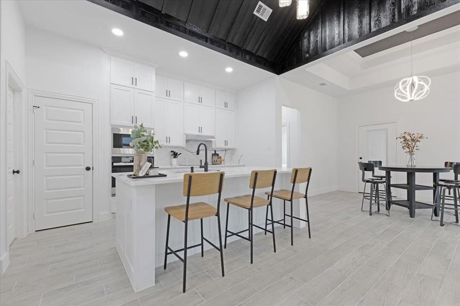 Kitchen featuring light countertops, visible vents, white cabinets, an island with sink, and a kitchen breakfast bar