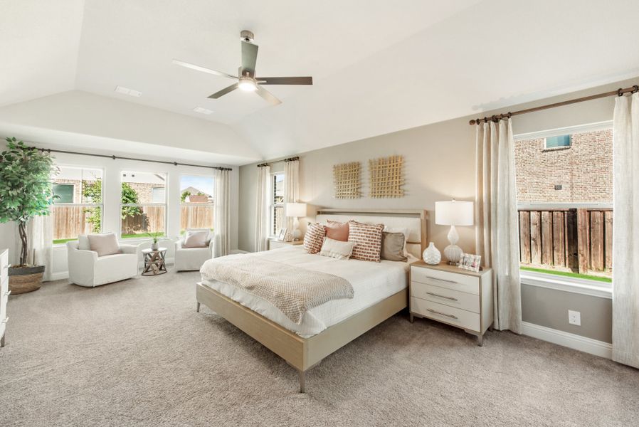 Spacious master bedroom with vaulted ceiling, ceiling fan, carpet floors, and large windows with natural light