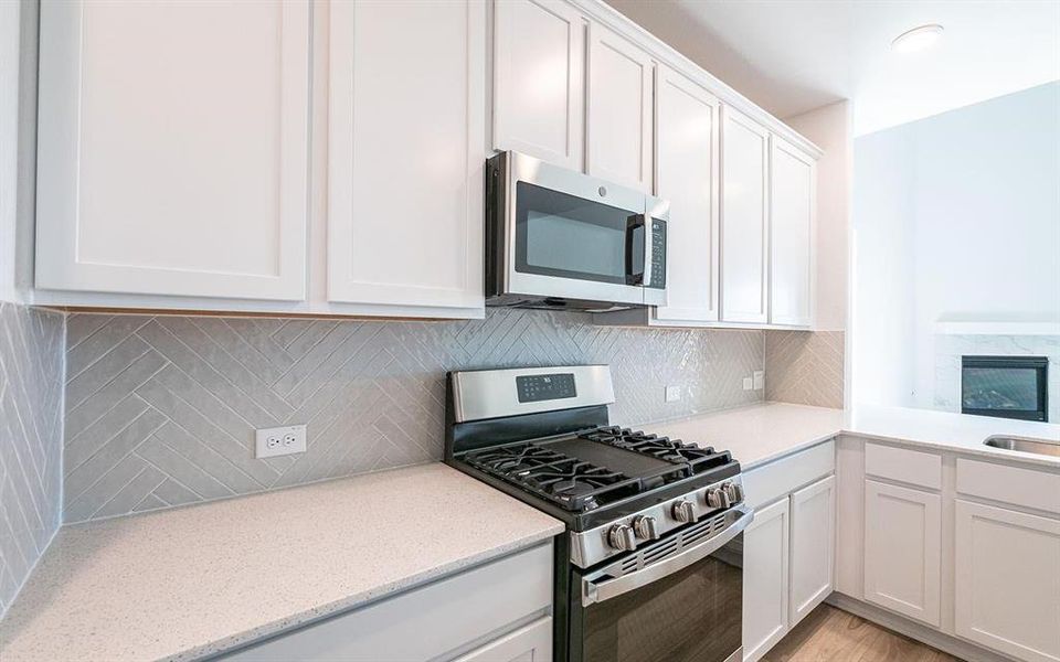 Kitchen with white cabinets, stainless steel appliances, decorative backsplash, and light hardwood / wood-style flooring
