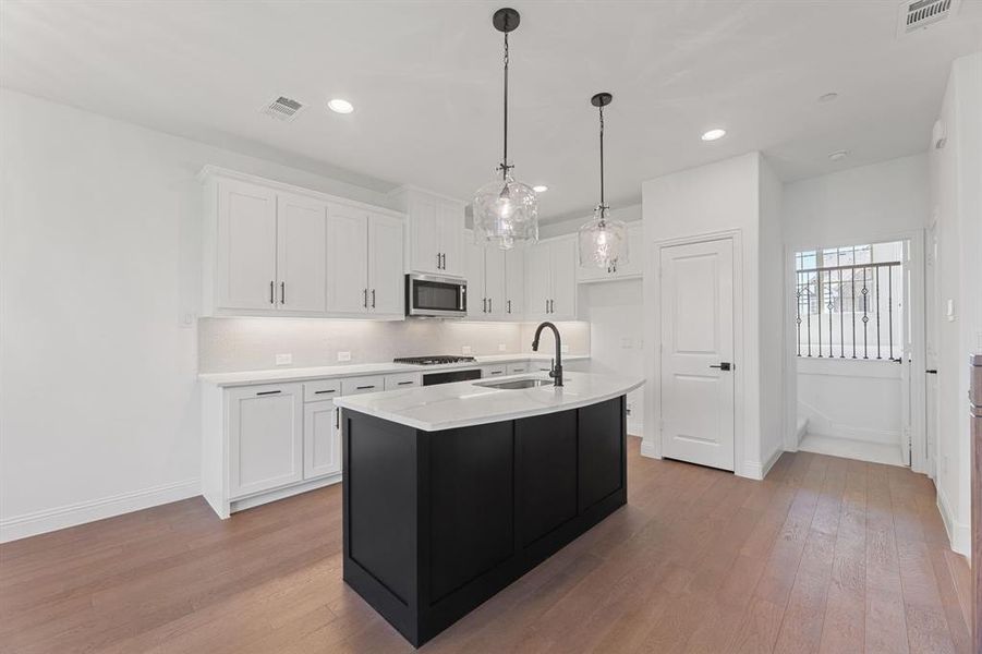 Kitchen with white cabinets, light wood-style floors, backsplash, hanging light fixtures, and recessed lighting Kitchen with white cabinets, light wood-style floors, backsplash, hanging light fixtures, and recessed lighting