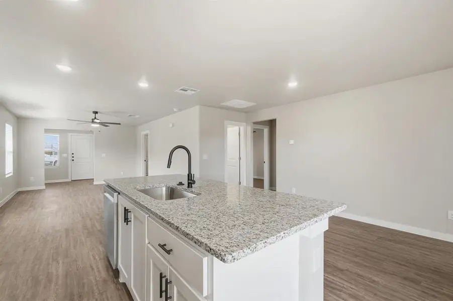 Kitchen with light wood-style flooring, a center island with sink, light stone countertops, white cabinets, and recessed lighting