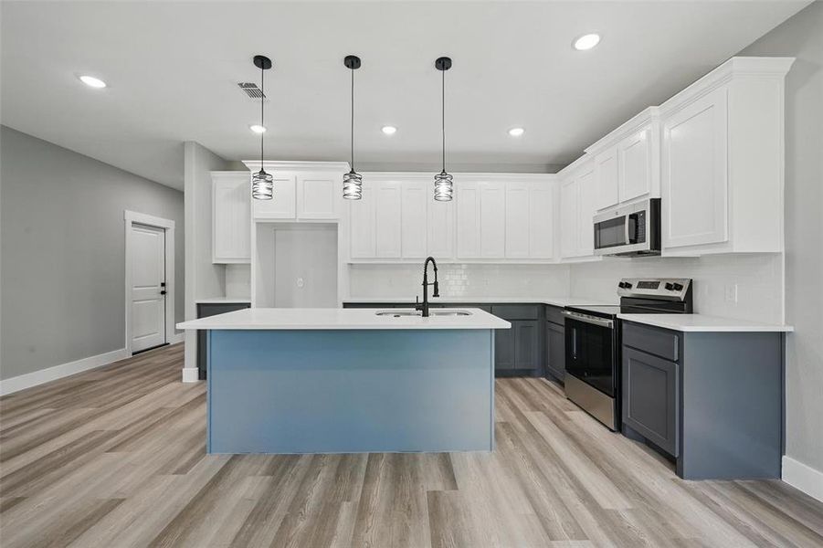 Kitchen with appliances with stainless steel finishes, a sink, gray cabinetry, light wood-style floors, and a center island with sink