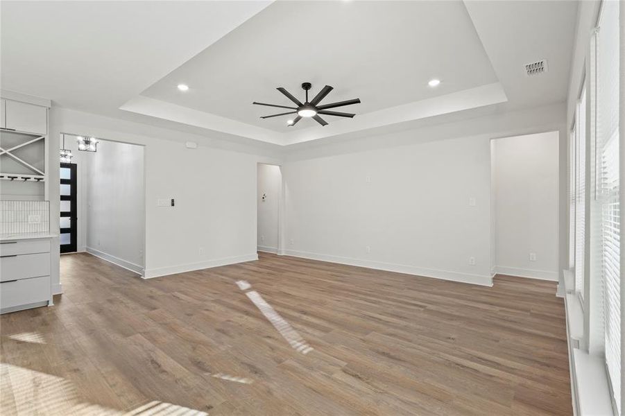 Unfurnished room with ceiling fan, visible vents, baseboards, light wood-type flooring, and a tray ceiling