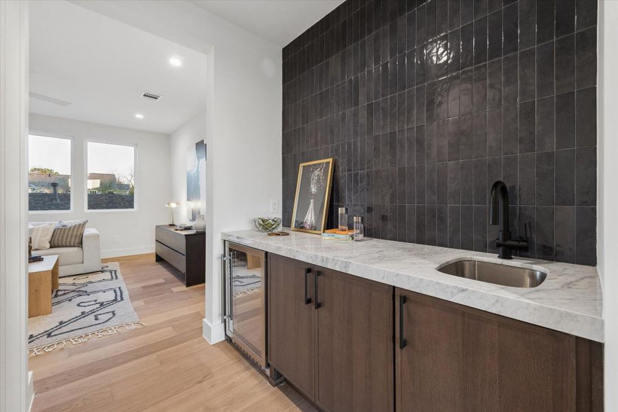 Wet bar conveniently located just outside the gameroom, featuring a 24” beverage refrigerator, ample storage, a polished Carrara marble countertop, and Italian porcelain tile.