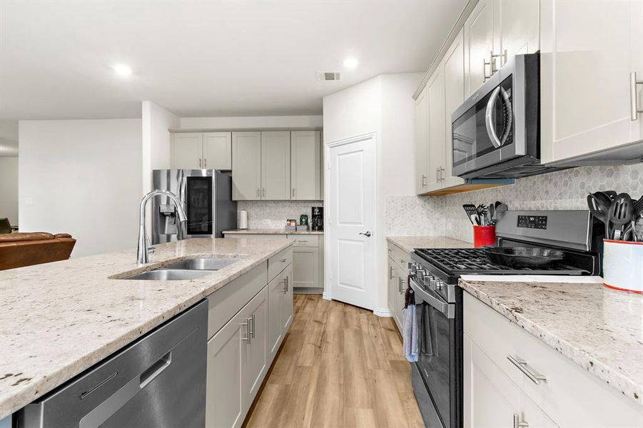 Kitchen with appliances with stainless steel finishes, light wood-type flooring, tasteful backsplash, light stone counters, and recessed lighting Kitchen with appliances with stainless steel finishes, light wood-type flooring, tasteful backsplash, light stone counters, and recessed lighting