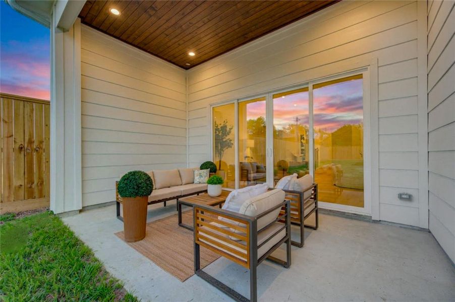 Covered back patio creates a seamless extension of the home’s living space, with expansive glass doors connecting directly to the interior. Warm wood-look ceiling details and recessed lighting elevate the setting, while the adjoining lawn provides additional outdoor space for relaxing, entertaining, or enjoying quiet evenings at home. Covered back patio creates a seamless extension of the home’s living space, with expansive glass doors connecting directly to the interior. Warm wood-look ceiling details and recessed lighting elevate the setting, while the adjoining lawn provides additional outdoor space for relaxing, entertaining, or enjoying quiet evenings at home.