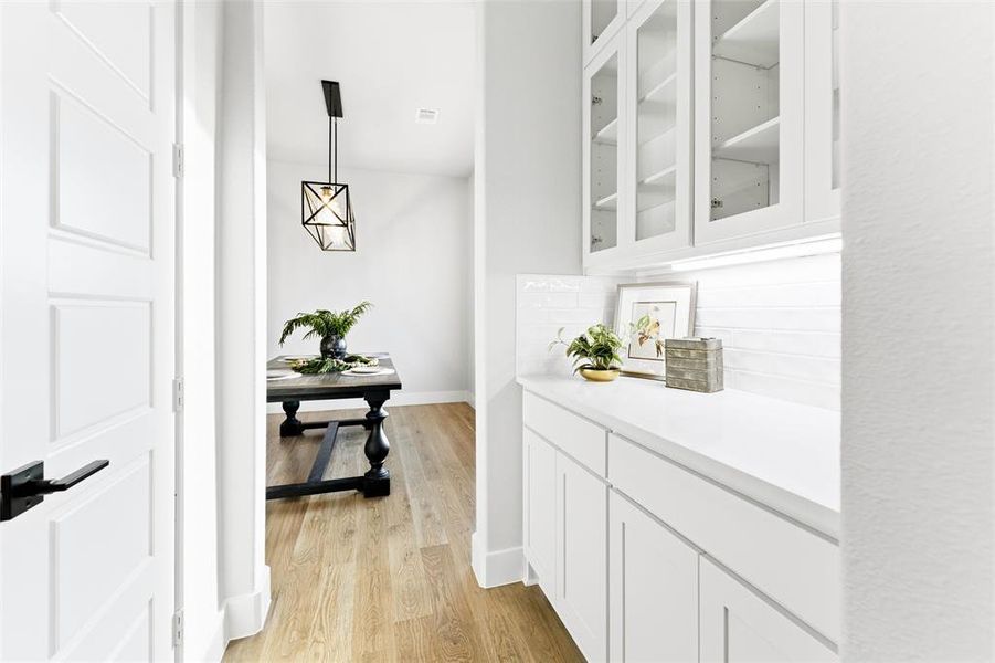 Bar with glass insert cabinets, white cabinetry, hanging light fixtures, tasteful backsplash, and light wood-style floors