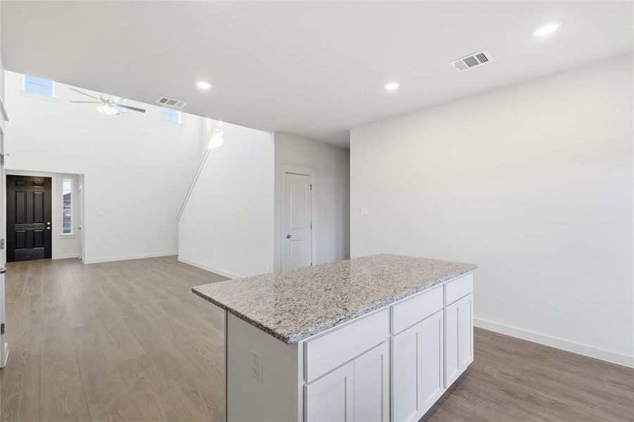 Open-concept living area featuring a kitchen island with a speckled countertop, white cabinetry, and wood-finish flooring Open-concept living area featuring a kitchen island with a speckled countertop, white cabinetry, and wood-finish flooring