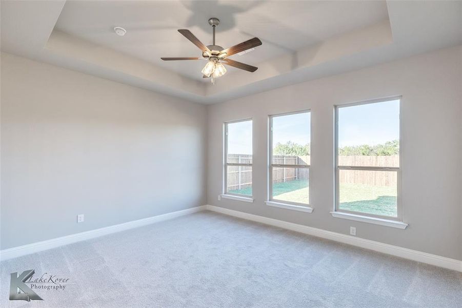 Unfurnished room featuring a tray ceiling, light colored carpet, and ceiling fan