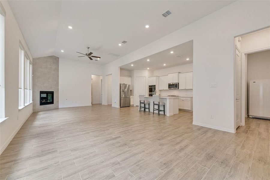 Unfurnished living room with ceiling fan, vaulted ceiling, recessed lighting, light wood-style flooring, and a fireplace Unfurnished living room with ceiling fan, vaulted ceiling, recessed lighting, light wood-style flooring, and a fireplace