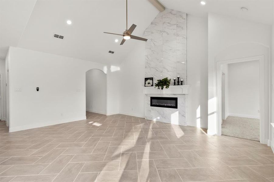 Unfurnished living room with beamed ceiling, a premium fireplace, high vaulted ceiling, and ceiling fan