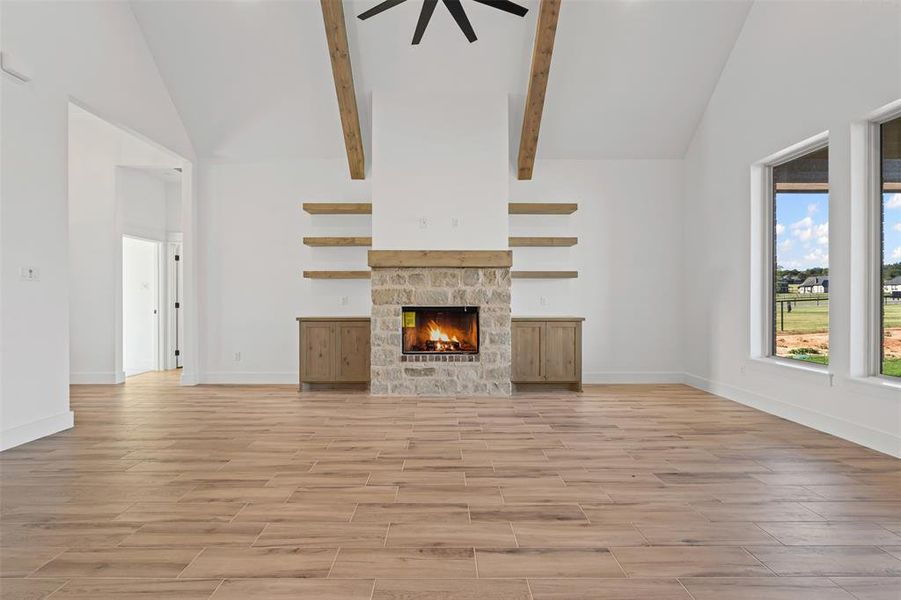 Unfurnished living room featuring high vaulted ceiling, wood tiled floors, a stone fireplace, a ceiling fan, and beam ceiling