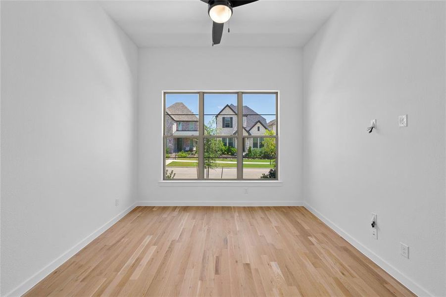 Room with wood-finish flooring, a contemporary ceiling fan, and a large window overlooking a residential street with stone and brick homes