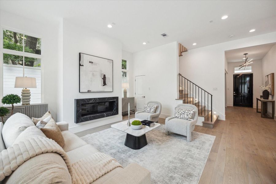 The expansive living room features an elegant fireplace with Nero Marquina detail, wrought iron stairway detail, LED integrated recessed lighting and Pella Lifestyle windows.