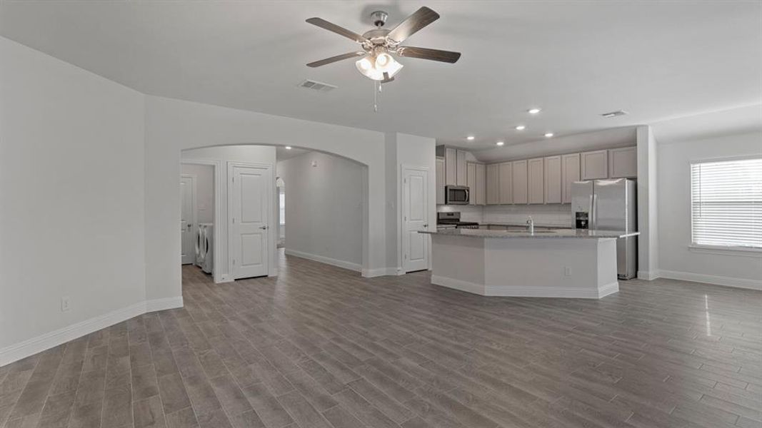 Kitchen featuring recessed lighting, an island with sink, arched walkways, open floor plan, and light stone countertops