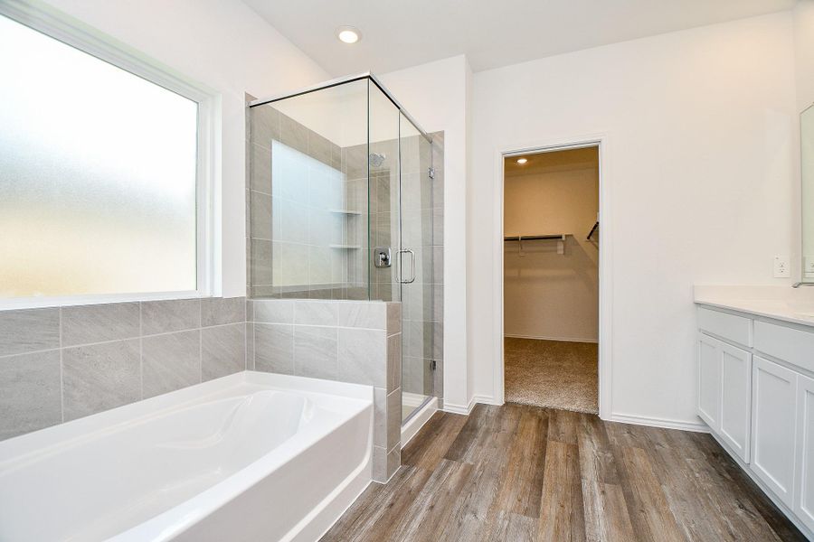 This photo showcases a modern bathroom featuring a spacious glass-enclosed shower, a large bathtub with tile surround, and a sleek vanity. The room is bright and airy, accentuated by a frosted window and elegant wood-look flooring. A doorway leads to a generously sized walk-in closet. This photo showcases a modern bathroom featuring a spacious glass-enclosed shower, a large bathtub with tile surround, and a sleek vanity. The room is bright and airy, accentuated by a frosted window and elegant wood-look flooring. A doorway leads to a generously sized walk-in closet.