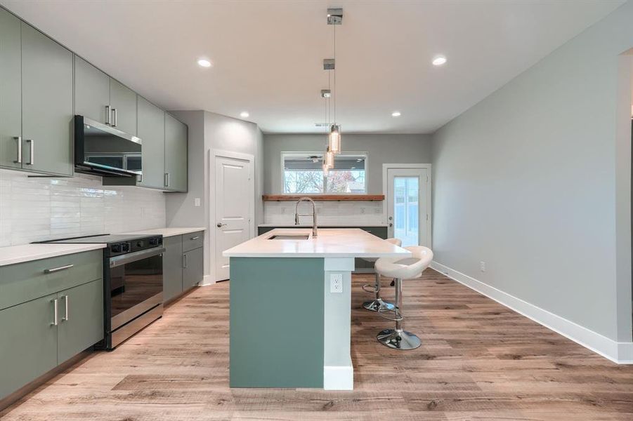 Kitchen featuring sink, stainless steel appliances, light hardwood / wood-style flooring, backsplash, and pendant lighting