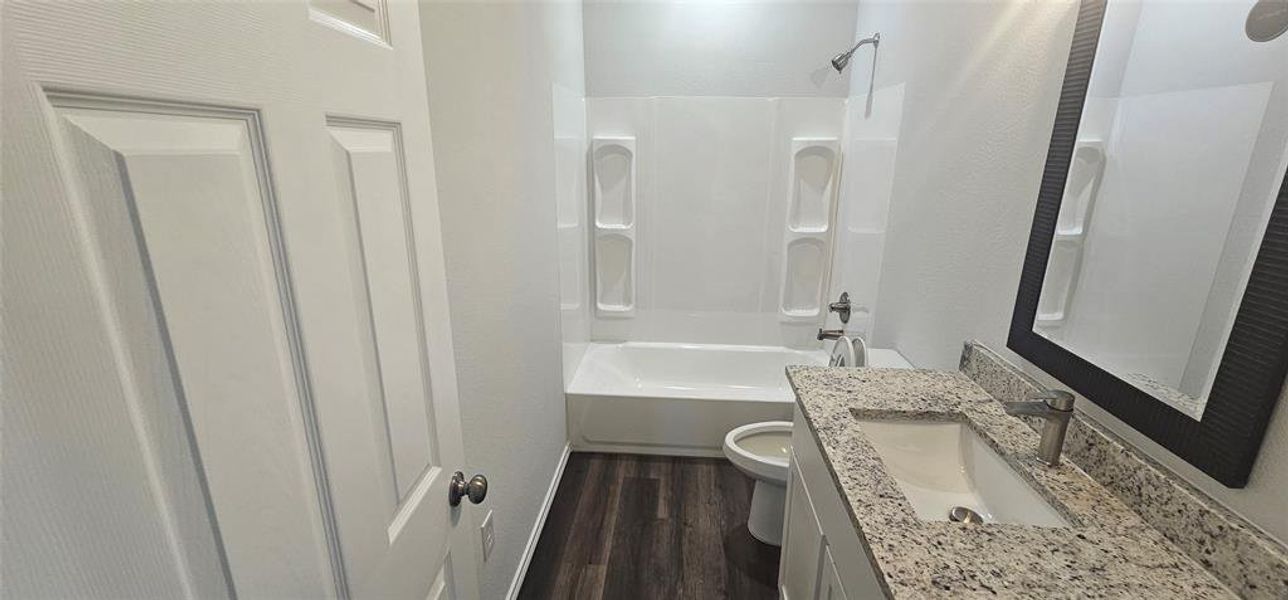 Full bathroom with dark wood-type flooring, bathtub / shower combination, vanity, and a textured wall